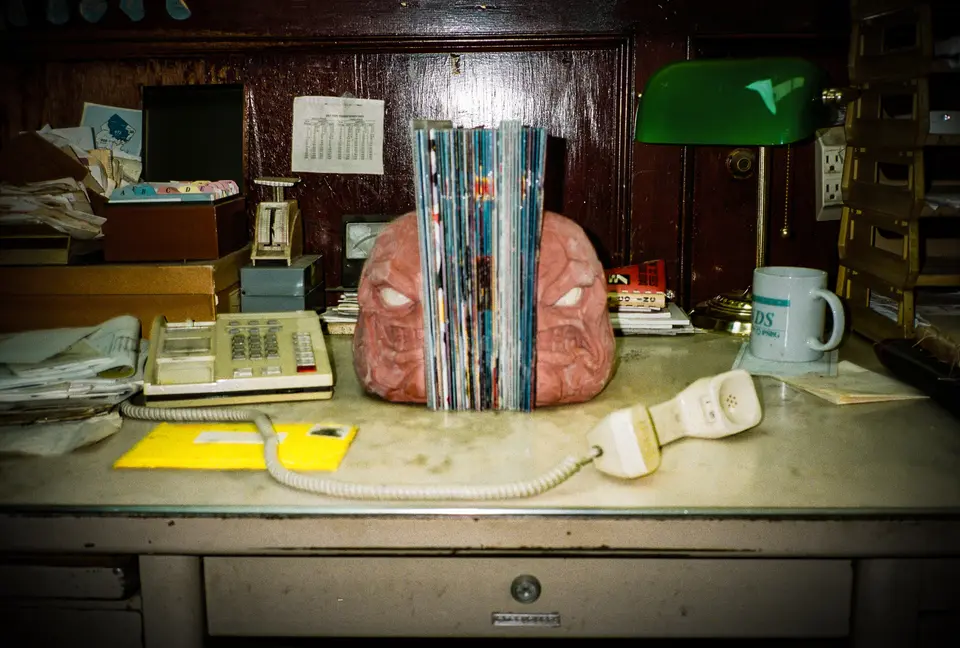 Clayface bookends on a cluttered office desk under a green banker lamp