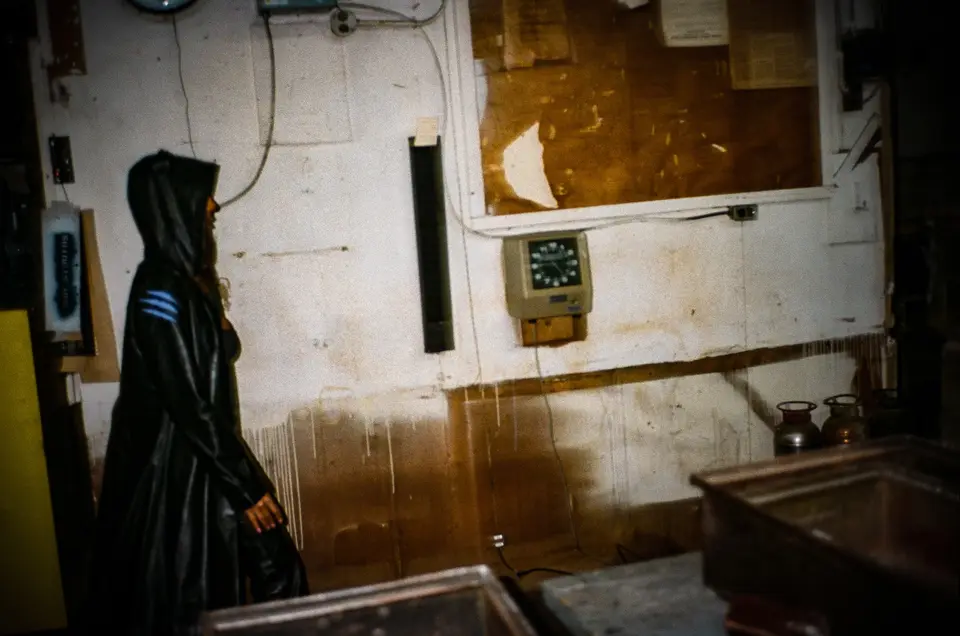 Hooded figure in the long Catwoman leather trench in a stained workshop