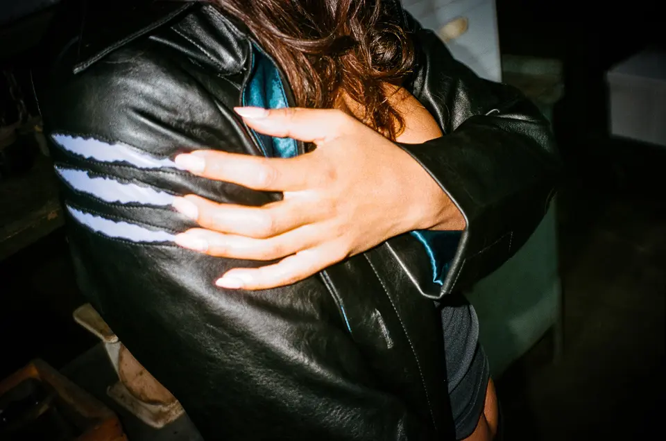 Hand on the shoulder of the black leather Catwoman trench with white claw stripes