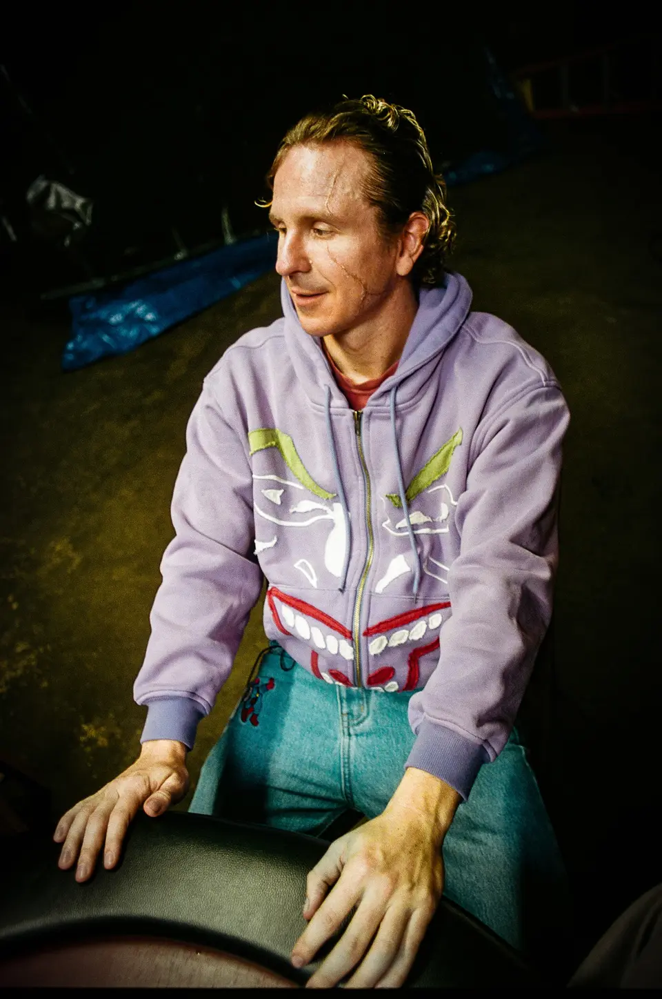 Man in the lilac Joker face hoodie leaning on a poker table