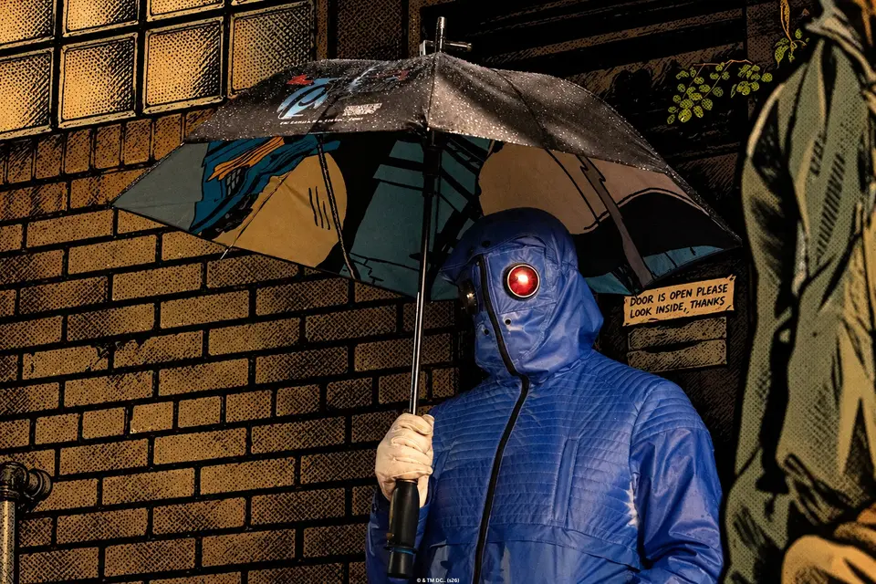 Mr. Freeze in a blue puffer and red goggles under a comic-print umbrella