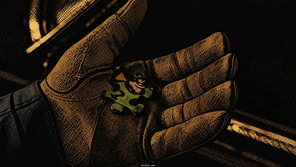Gloved hand holding a single green Riddler puzzle piece